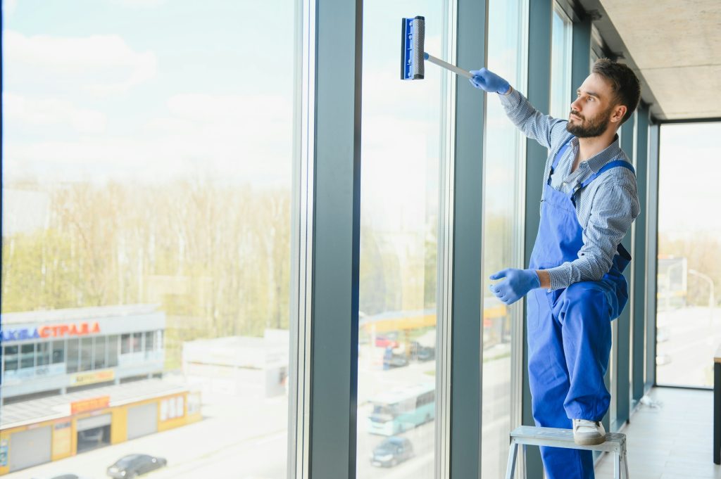 Male professional cleaning service worker in overalls cleans the windows and shop windows